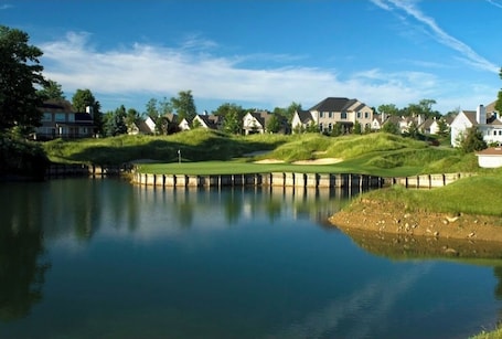 A serene lakeside view with a golf course, houses, and a wooden dock.
