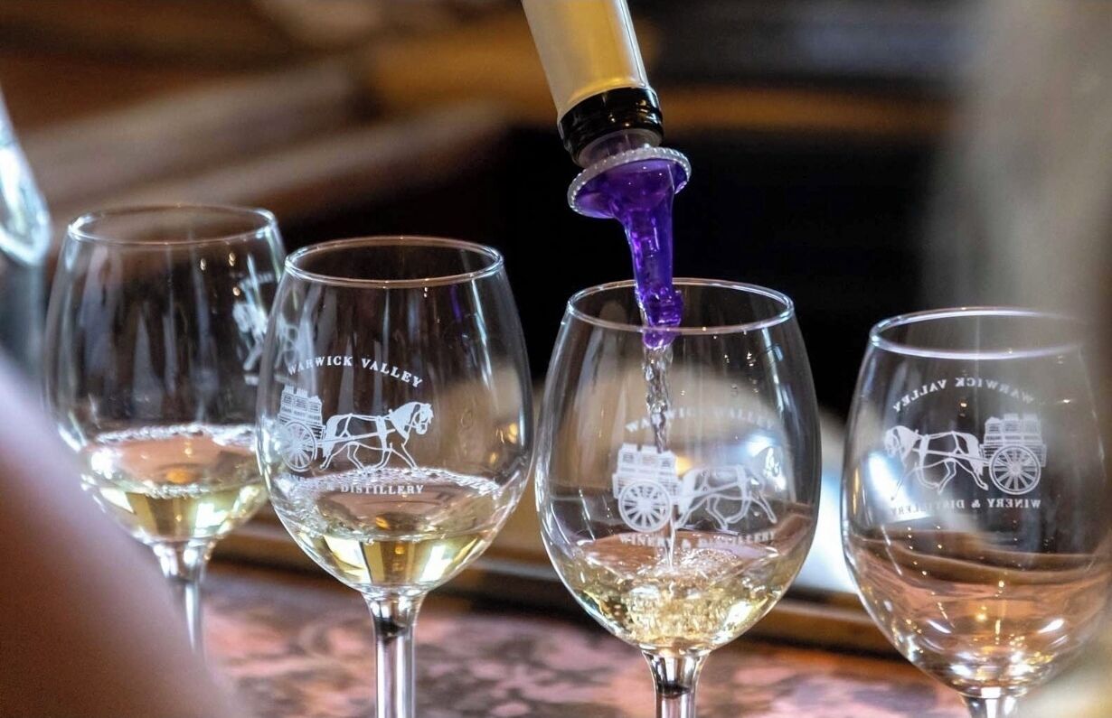 Four wine glasses with a horse and carriage logo, one glass being filled with a purple liquid.