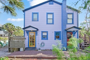Ein zweigeschossiges Haus mit blauer Fassade, einer Veranda und einer roten Tür.