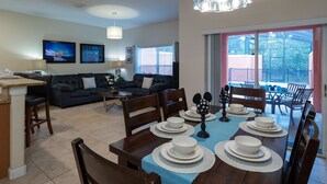 A modern living room with a dark-colored sofa, a dining table set with white plates and bowls, and a large window with a view of greenery.