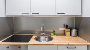 Una cocina con un lavamanos de acero inoxidable, una placa de inducción negra, encimeras de madera y armarios arriba.