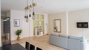 Una sala de estar moderna con un sofá gris, una mesa de comedor con sillas, una planta y una estantería.