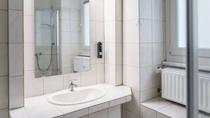 Un baño moderno con un lavamanos blanco, cabina de ducha con mampara de vidrio y un espejo grande.