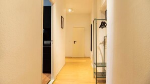 A narrow hallway with a wooden floor, a door at the end, and a metal rack with hangers on the right.