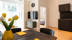 Un espacio habitable moderno con comedor, televisor montado en la pared, área de cocina y una cama al fondo.