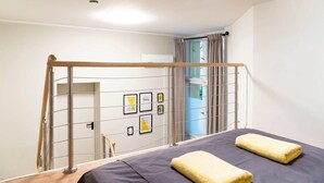 A bedroom with a bed, a metal ladder, a door, and a window with curtains.