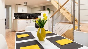 A modern kitchen with white cabinets, a black backsplash, and a wooden staircase.