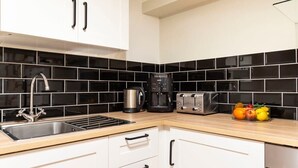 A modern kitchen with white cabinets, black tiled backsplash, stainless steel appliances, and a wooden countertop.