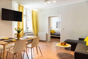 A modern living room with a dining area, a sofa, and a TV mounted on the wall. - Cosy Two BR plus Self Checkin (Berlin)
