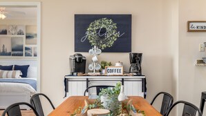 A dining area with a wooden table, chairs, a coffee station, and a wall-mounted sign. - Gorgeous Beach Club Condo! Spectacular Views! - RAMBL ONE (Dauphin Island)
