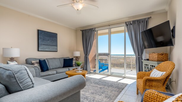A modern living room with a grey sofa, a wicker chair, a flat-screen TV, and a balcony with a view. - Gorgeous Beach Club Condo! Spectacular Views! - RAMBL ONE (Dauphin Island)