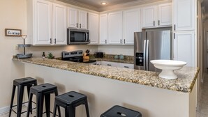 A modern kitchen with white cabinets, stainless steel appliances, granite countertops, and bar stools. - Gorgeous Beach Club Condo! Spectacular Views! - RAMBL ONE (Dauphin Island)