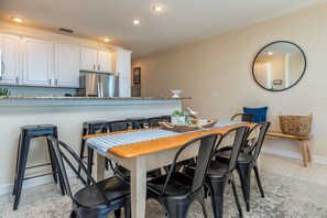 Una cocina moderna con armarios blancos, electrodomésticos de acero inoxidable y un comedor con mesa de madera y sillas negras.