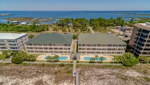 An aerial view of a hotel with multiple swimming pools, a beach area, and a view of the ocean and a bridge in the distance. - Gorgeous Beach Club Condo! Spectacular Views! - RAMBL ONE (Dauphin Island)