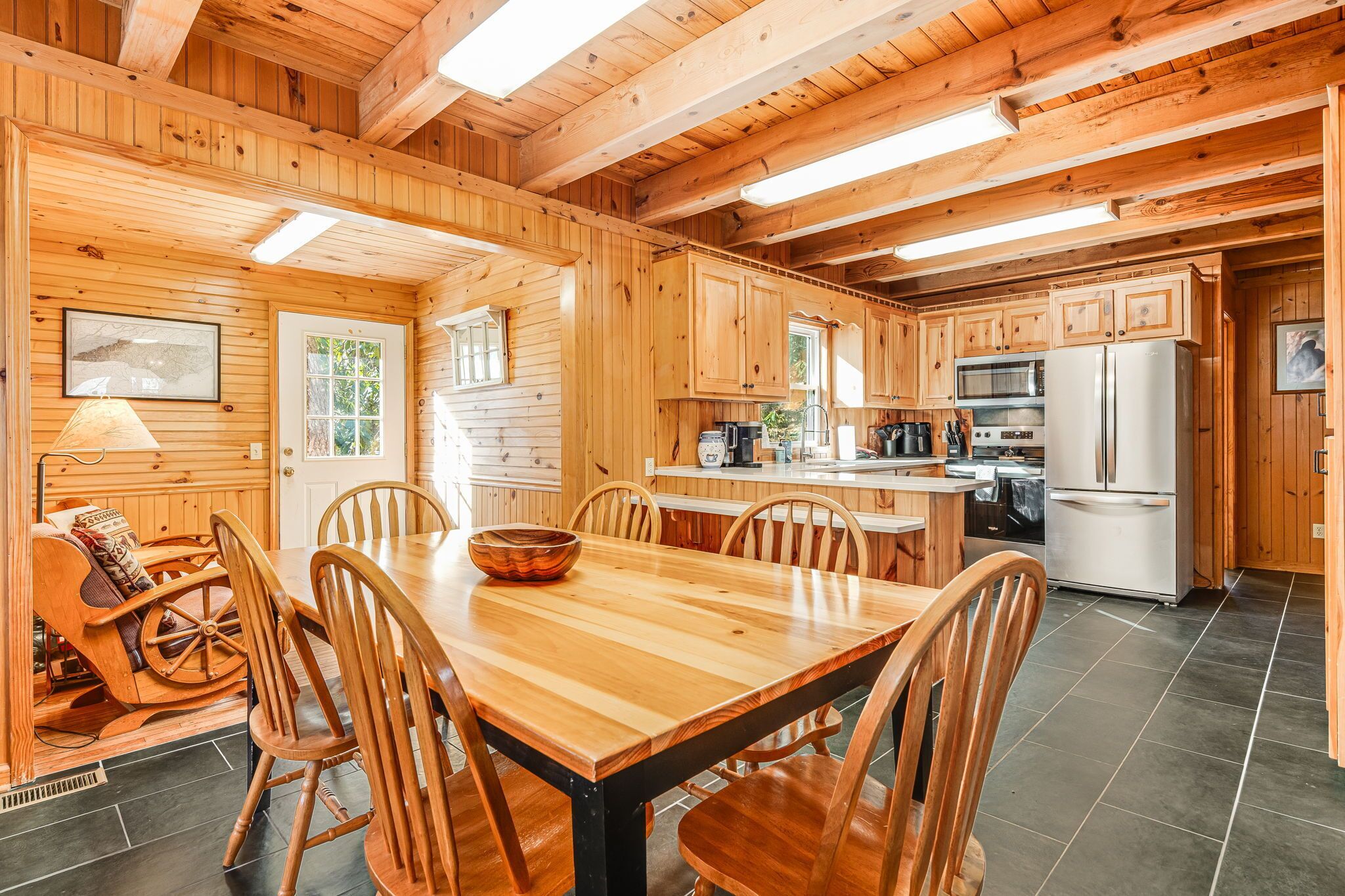 A wooden cabin interior with a dining area, kitchen, and a cozy seating area with a rocking chair.