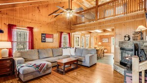 Interior acogedor de una cabaña de madera con un gran techo de madera, una chimenea, un conjunto de sofás y una zona de comedor.