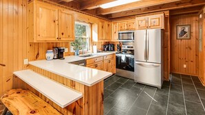 Cocina de cabaña de madera con una isla central, un refrigerador, estufa y un lavamanos.