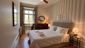 A bedroom with a large bed, a dresser, a mirror, and a window with curtains.