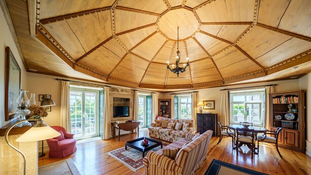A spacious living room with a wooden ceiling, a fireplace, a sofa, a coffee table, and a dining area with a table and chairs.