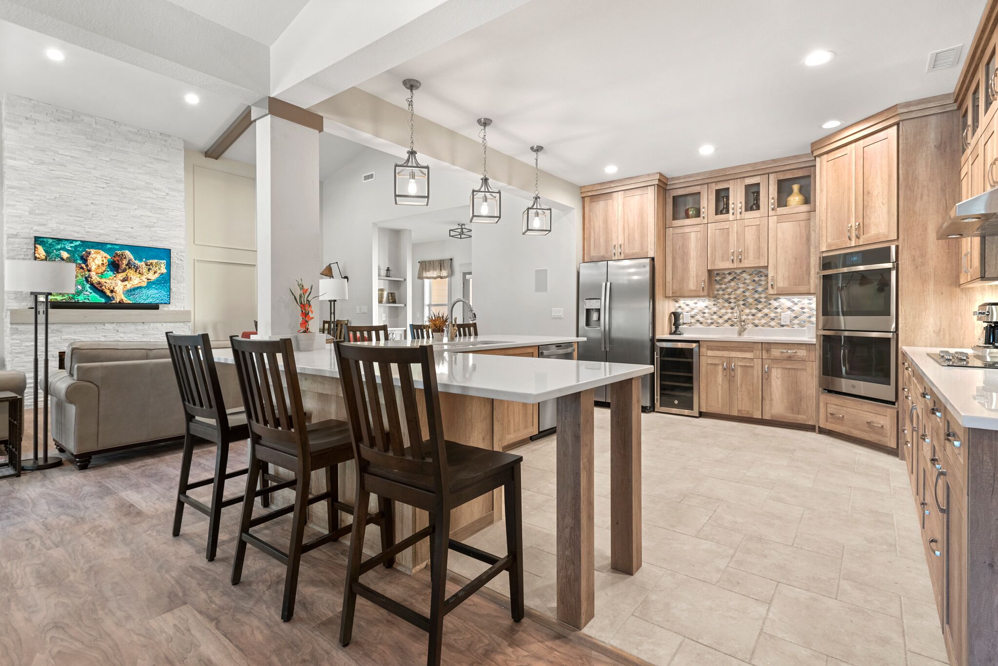 A modern kitchen with wooden cabinets, a central island, and a dining area with chairs.