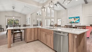 A spacious kitchen with a large island, wooden cabinets, and a stainless steel dishwasher. - Breeze The Day: Saltwater Pool, Pool Table, Spa (Corolla)