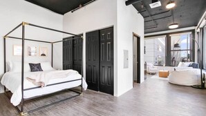 Une chambre moderne avec un lit à baldaquin, un dressing et une vue sur la ville grâce à de grandes fenêtres.