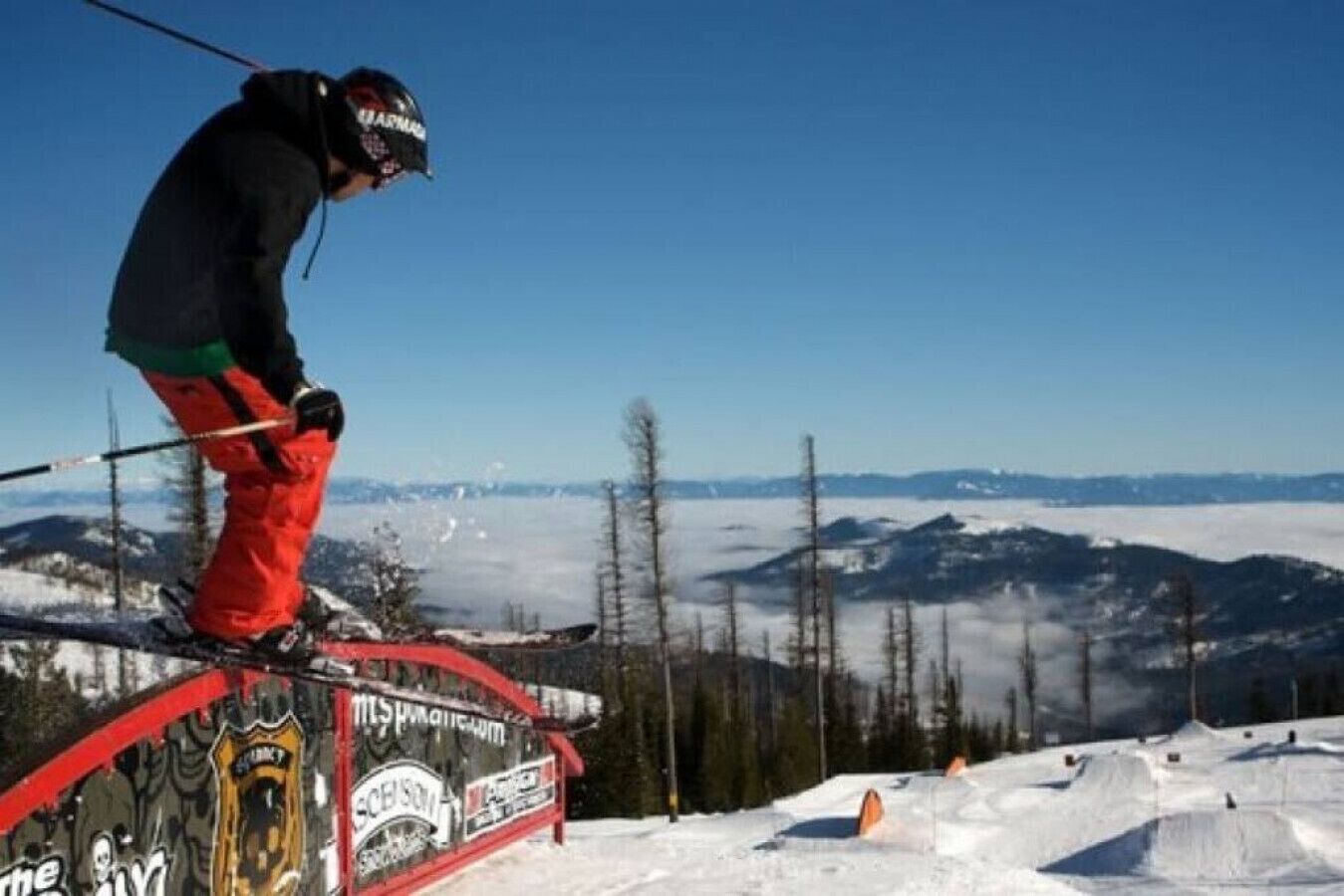Une personne fait du ski sur une pente enneigée, avec une vue dégagée sur les montagnes et les arbres en arrière-plan.