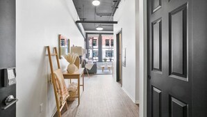 A hallway with a wooden floor, a black door, and a view into a living area with a sofa and a table. - Urban Modern Living Downtown w/ Free Coffee & WiFi (Spokane)