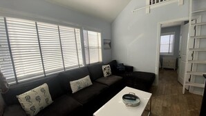 Una sala de estar con un sofá marrón oscuro, una mesa de centro blanca y una escalera que lleva a un nivel superior.