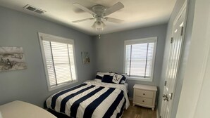 Un dormitorio con cama, mesitas de noche, ventilador de techo y una puerta.