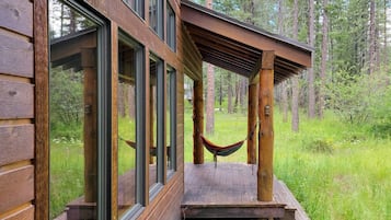 Una cabaña de madera con ventanas amplias, una hamaca y una terraza con vistas a un bosque.
