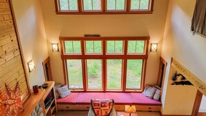 A room with a large window, a built-in bench, a fireplace, and a wall-mounted light fixture. - Triple J Cabin (Mazama)