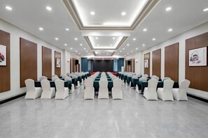 A conference room with rows of tables and chairs, a stage, and a long table with red chairs. - Sports International Hotel (Kunshan)