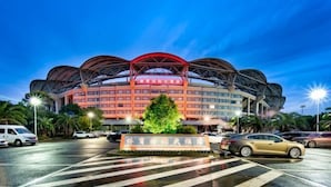 A hotel with a distinctive red and white facade, a large central entrance, and a parking lot with several cars. - Sports International Hotel (Kunshan)
