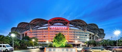 A hotel with a distinctive roof structure, multiple floors, and a parking area with cars.