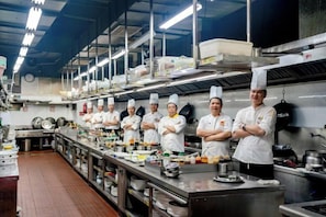 A professional kitchen with chefs standing in a row, stainless steel appliances, and a long counter. - Sports International Hotel (Kunshan)