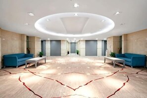 A spacious lobby with a modern design, featuring a central seating area with sofas and a patterned carpet. - Sports International Hotel (Kunshan)