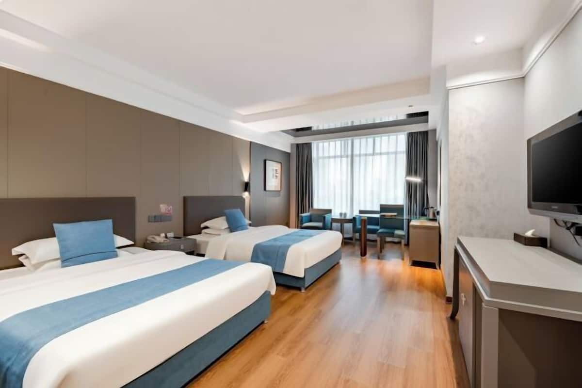 A hotel room with two beds, a desk, a television, and a seating area with a view of the city.