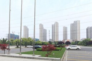 A parking lot with cars, a grassy area with trees, and tall buildings in the background. - Sports International Hotel (Kunshan)