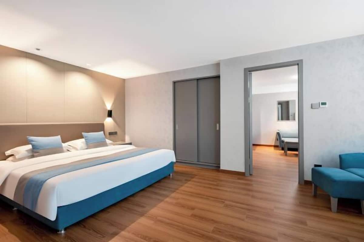 A modern hotel room with a large bed, a separate seating area, and a wardrobe.