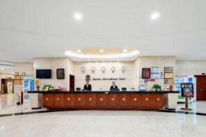 A hotel reception area with a reception desk, a clock, and a sign that reads 'Sports International Hotel'. - Sports International Hotel (Kunshan)
