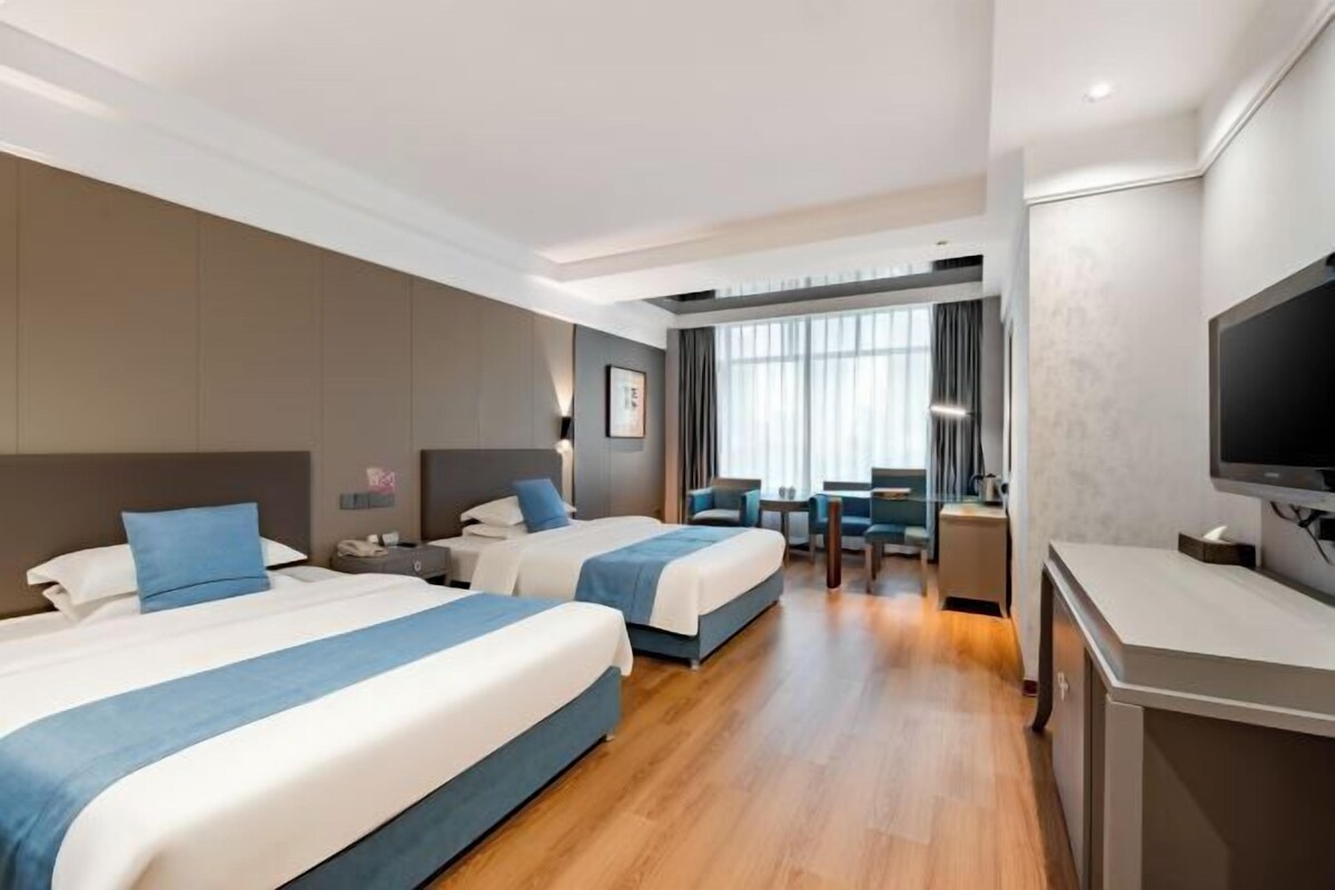 Ein Hotelzimmer mit zwei Betten, einem Schreibtisch, einem Fernseher und einer Sitzecke mit Blick ins Freie.