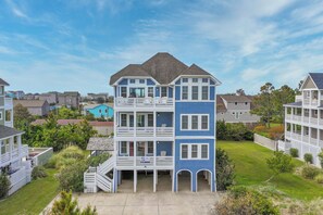 A two-story residential building with a balcony on the upper floor, surrounded by greenery and other houses. - Oceanview Home w/ Private Pool, Elevator, Hot Tub, Media Room, Game Rooms (Salvo)