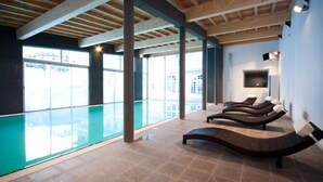 A modern indoor pool area with a glass wall, wooden ceiling beams, and lounge chairs. - Village vacances Neaclub - La Pulka (Valloire)