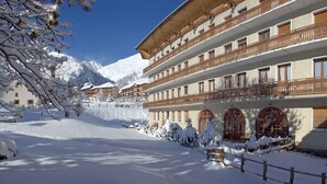 A multi-story hotel with balconies and large windows, surrounded by snow-covered mountains. - Village vacances Neaclub - La Pulka (Valloire)