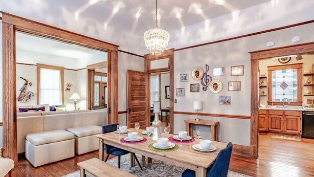 Un coin repas avec une table en bois dressée pour quatre personnes, un lustre et une vue sur la cuisine.