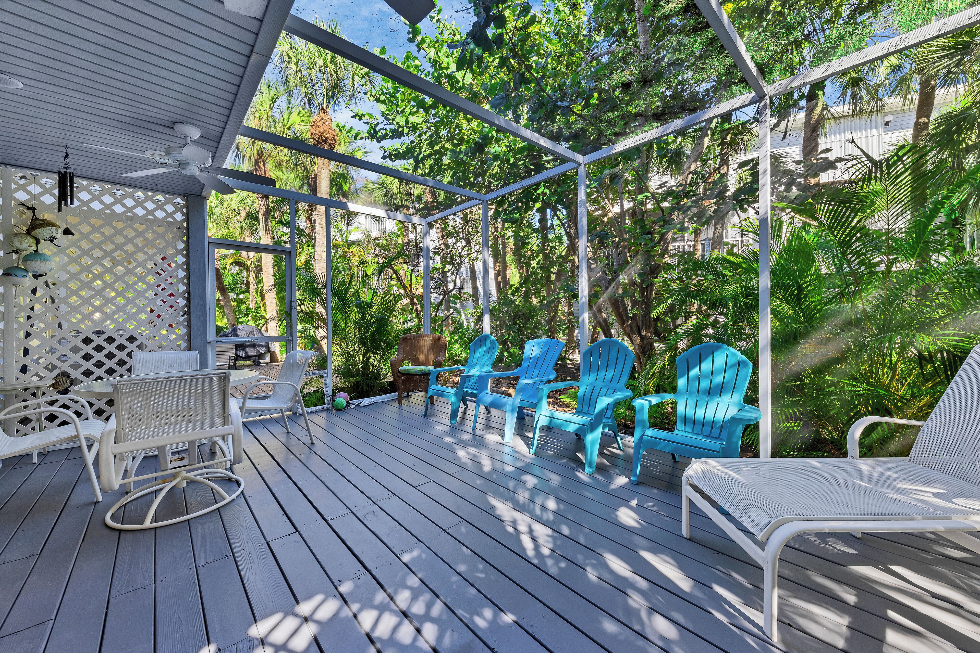 Une terrasse extérieure couverte, agrémentée de chaises Adirondack bleues, de meubles en osier blancs et d’une balançoire blanche.