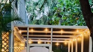 A covered outdoor seating area with string lights, a table, chairs, and an umbrella. - 2-Min Walk to Holmes Beach - Walk to Shops & Dining - Quiet Tropical Townhouse (Holmes Beach)