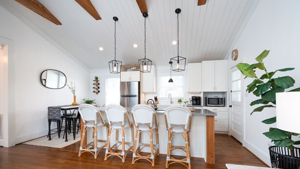 A modern kitchen with white cabinets, a central island with bar stools, a refrigerator, and a microwave. - Boho-Chic South CLT Oasis ★ Custom Home ★ Sleeps 6 (Charlotte)
