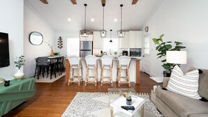A spacious living room with a wooden ceiling, a dining area with wicker chairs, and a kitchen with modern appliances. - Boho-Chic South CLT Oasis ★ Custom Home ★ Sleeps 6 (Charlotte)